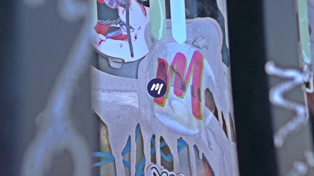 Ein Aufkleber mit dem mehappy-Logo m klebt zwischen Graffitis, Streetart und anderen Aufklebern, vor einem Gitter.